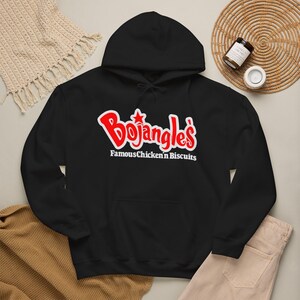 May include: A black hooded sweatshirt featuring the red and white Bojangles logo on the chest. The graphic includes the text Bojangles with a star above the letter j, followed by the white text Famous Chicken 'n Biscuits below the logo.