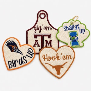 May include: Four embroidered patches with cream-colored fabric bases. One heart-shaped patch features a bird head and 'Birds up', another heart-shaped patch shows a longhorn and 'Hook 'em', a tag-shaped patch says 'gig 'em' with 'ATM', and a shell-shaped patch says 'shakas up'.