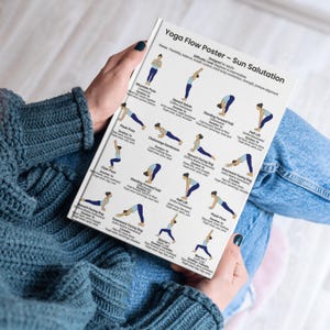 May include: A white yoga flow poster titled "Yoga Flow Poster - Sun Salutation" held by a person. The poster features illustrated yoga poses with text descriptions. The poster's focus is on flexibility, balance, breath control, and strength.