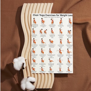 Peut inclure: Une affiche blanche avec le texte "Chair Yoga Exercises for Weight Loss" et des illustrations d'exercices de yoga sur chaise. L'affiche est pr&eacute;sent&eacute;e sur un cadre en bois clair, avec une branche de coton au premier plan. Le fond est en tissu marron.