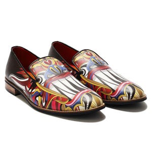 May include: A pair of slip-on shoes with a striking, abstract pattern in red, yellow, blue, and white. The shoes have brown soles and red interiors. The shoes are made of leather. The design is eye-catching and bold.