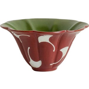 Può includere: Una ciotola decorativa in ceramica con bordo smerlato. L'esterno è rosso scuro con disegni bianchi a forma di foglia e l'interno è verde unito. La ciotola ha una forma svasata unica.