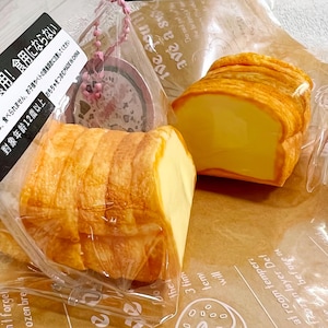 Può includere: Due fette di pane finto in un sacchetto di plastica trasparente. Il pane è giallo e marrone e ha una consistenza realistica. Il sacchetto ha un'etichetta rosa e bianca che dice "不可食用! 食用にならない", che si traduce in "Non commestibile! Non mangiare!" in inglese.