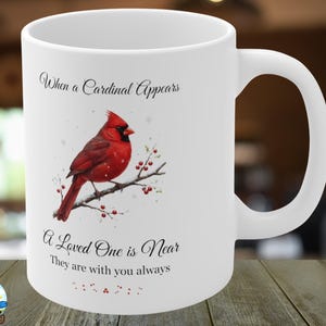 Pode incluir: Caneca de cer&acirc;mica branca com um cardeal vermelho num galho. A caneca tem o texto: "Quando um cardeal aparece, um ente querido est&aacute; perto, eles est&atilde;o sempre com voc&ecirc;."