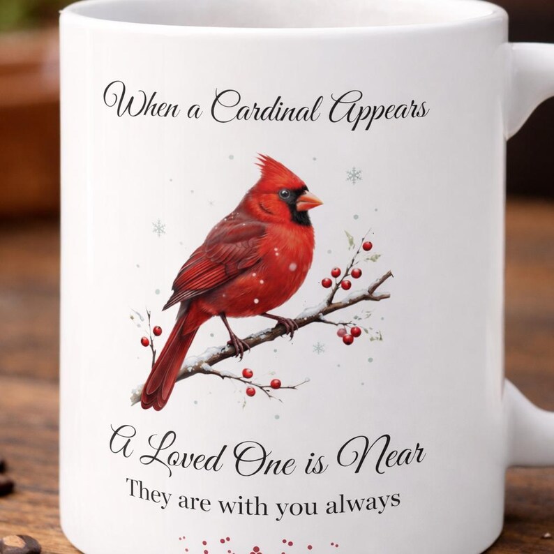 Pode incluir: Caneca de cer&acirc;mica branca com um cardeal vermelho vibrante empoleirado em um galho com bagas. A caneca tem o texto "When a Cardinal Appears, A Loved One is Near, They are with you always."