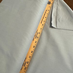 May include: A light blue fabric roll with a wooden ruler measuring 21 inches. The ruler has text that reads "Do you have it all covered?" and "Primer Tape Caulk". The fabric is folded over on the right side.