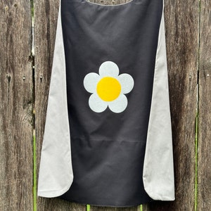 May include: Black cape with a white daisy with a yellow center. The cape has gray fabric on the edges.