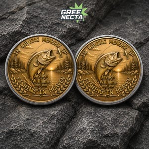 May include: Two circular gold-toned commemorative coins featuring a raised relief of a bass fish jumping out of water. The text reads IN LOVING MEMORY OF Jayden Williams 1969-2026 FISHING IN HEAVEN, surrounded by a forest landscape and laurel leaf borders.