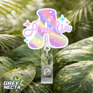 May include: A badge reel featuring the name "Amelia" in a cursive font. The letter "A" is filled with a rainbow galaxy design and outlined in white. The badge reel has a clear plastic clip and a retractable cord.