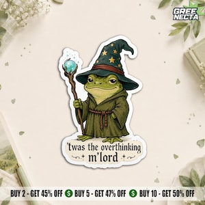 May include: A die-cut sticker featuring a green frog dressed as a wizard in a dark green robe and a pointed hat with yellow stars. The frog holds a wooden staff topped with a glowing blue orb. Below the frog, text reads: 'twas the overthinking m'lord'.