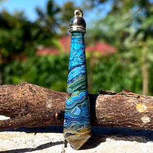 May include: A tapered, faceted pendant made of banded blue, green, and brown stone. The stone features intricate, swirling patterns of deep azure, teal, and earthy tan layers. It is topped with a polished silver-toned metal bail for hanging.