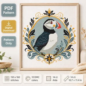 Puede incluir: Un patrón de punto de cruz con un frailecillo centrado en un marco ovalado ornamentado. El diseño utiliza tonos negros, blancos, naranjas y azules. Las etiquetas indican que es un patrón digital PDF de 150 por 160 puntos y 10 colores.