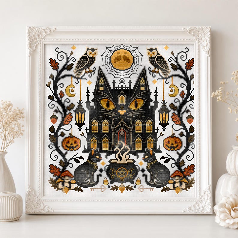 K&ouml;nnte beinhalten: Ein gerahmtes Kreuzstichbild mit einem schwarzen, katzenf&ouml;rmigen Spukhaus mit leuchtend gelben Augen. Das Design umfasst Eulen, K&uuml;rbisse, einen Kessel und einen Vollmond, alles im Halloween-Thema. Das Kunstwerk ist in einem wei&szlig;en, verzierten Rahmen gerahmt.