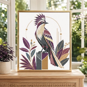 May include: A framed cross-stitch pattern featuring a stylised bird with a crest, rendered in shades of deep purple, charcoal grey, and cream. The bird is perched on a geometric block, surrounded by abstract leaf motifs and thin gold lines.