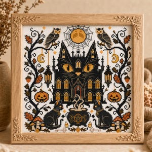 K&ouml;nnte beinhalten: Ein gerahmtes Kreuzstichbild mit einem schwarzen, katzenf&ouml;rmigen Spukhaus mit orangefarbenen Augen. Das Design umfasst Eulen, K&uuml;rbisse und einen Vollmond, alles vor einem wei&szlig;en Hintergrund. Der Rahmen ist aus hellem Holz.