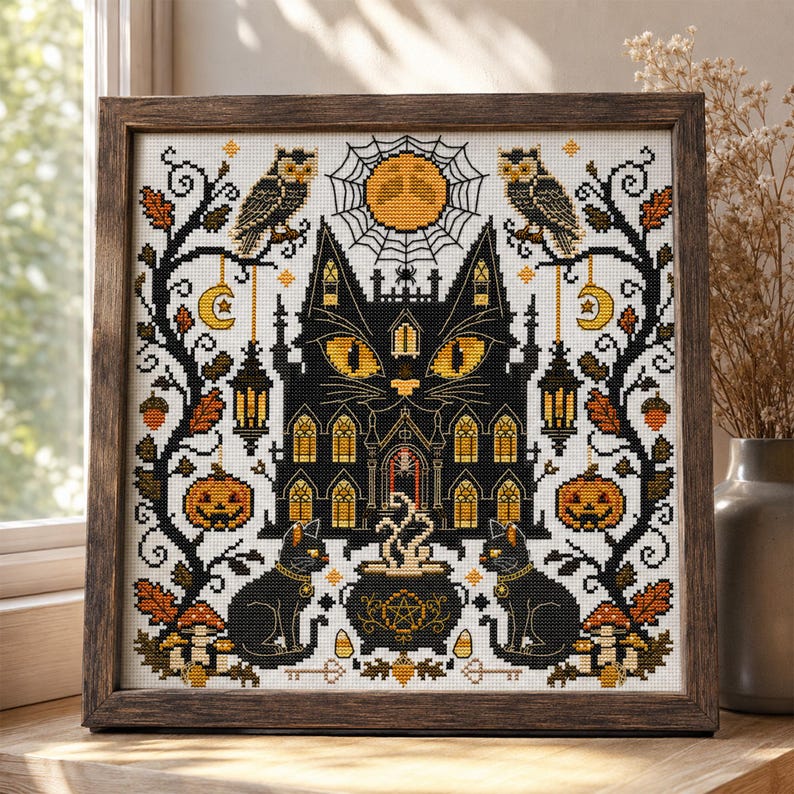 K&ouml;nnte beinhalten: Kreuzstich-Kunstwerk in einem Holzrahmen. Das Design zeigt ein schwarzes katzenf&ouml;rmiges Spukhaus mit leuchtend gelben Augen, flankiert von Eulen, K&uuml;rbissen und schwarzen Katzen. Ein Vollmond und ein Spinnennetz befinden sich im Hintergrund. Die Farbpalette umfasst Schwarz, Orange und Wei&szlig;.