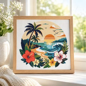 May include: A square cross-stitch embroidery in a light wood frame depicting a tropical beach scene at sunset. The design features palm trees, a breaking ocean wave, and a sandy shore, framed by vibrant red, white, and yellow hibiscus flowers.