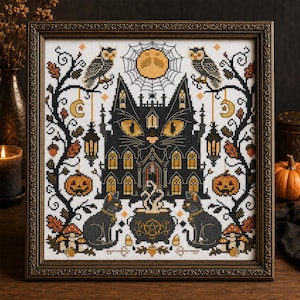 K&ouml;nnte beinhalten: Gerahmte Kreuzstichkunst mit einem schwarzen katzenf&ouml;rmigen Spukhaus mit leuchtend gelben Augen. Das Design umfasst Eulen, K&uuml;rbisse, einen Vollmond und einen Kessel, alles im Halloween-Thema. Der Rahmen ist dunkelbraun und verziert.