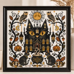 May include: Cross-stitch art in a black frame. The design features a black cat-shaped haunted house with yellow eyes, surrounded by owls, pumpkins, and a full moon. A cauldron steams between two black cats. The artwork has a Halloween theme.