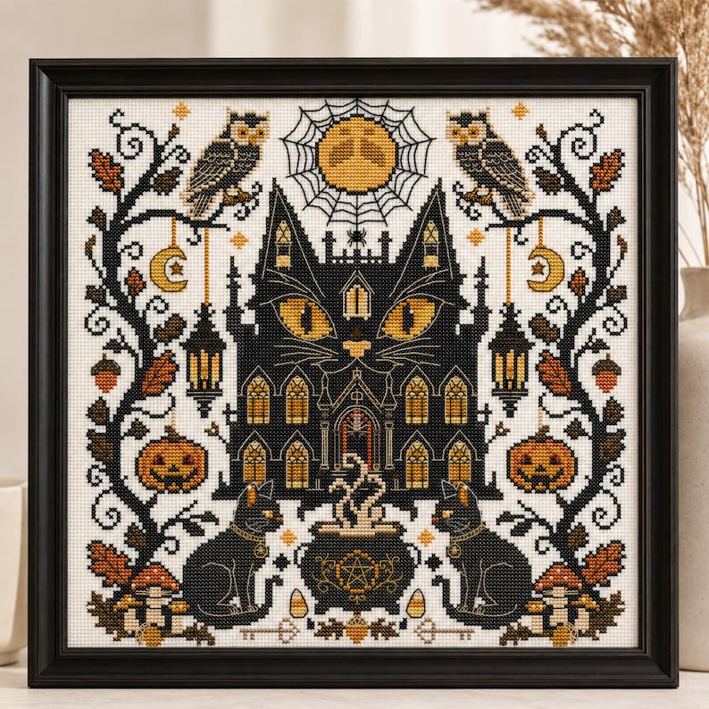 K&ouml;nnte beinhalten: Gerahmtes Kreuzstich-Kunstwerk mit Halloween-Motiv. Das Design zeigt ein schwarzes katzenf&ouml;rmiges Spukhaus mit gelben Augen, umgeben von Eulen, K&uuml;rbissen und einem Vollmond. Ein dampfender Kessel befindet sich zwischen zwei schwarzen Katzen.
