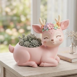 May include: A pink deer-shaped planter with a smiling face and a crown of colorful flowers. The planter is filled with a variety of succulents. The deer is resting on its front legs, and the overall design is whimsical and charming.
