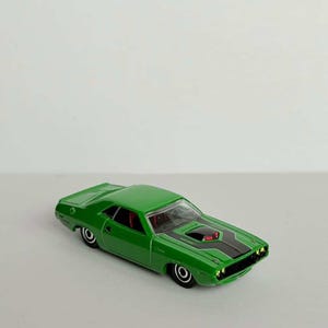 Peut inclure: Une voiture miniature verte avec des bandes noires sur le capot. La voiture a un intérieur rouge et des roues noires. La voiture miniature est une voiture de collection.