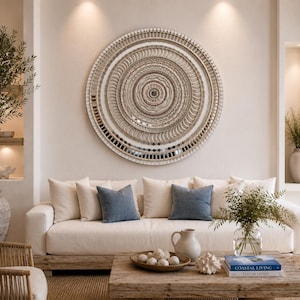 May include: A large circular wall art piece featuring concentric rings of textured beige, cream, and metallic silver elements. The design includes intricate patterns, small reflective mirror tiles, and a layered structure that creates a dimensional effect.