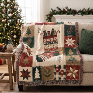 Könnte beinhalten: Eine gewebte Wohndecke mit Patchwork-Design und Weihnachtsmotiven, darunter ein großer zentraler Weihnachtsstrumpf gefüllt mit Büchern und Zuckerstangen, umgeben von Quadraten mit Tannenbäumen, Sternen, Beeren und Fäustlingen in Rot, Grün und Creme.
