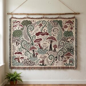 May include: A rectangular woven wall tapestry featuring a detailed botanical pattern of various mushrooms, ferns, and swirling foliage in shades of deep red, forest green, and cream. The textile has a fringed edge and hangs from a wooden rod.