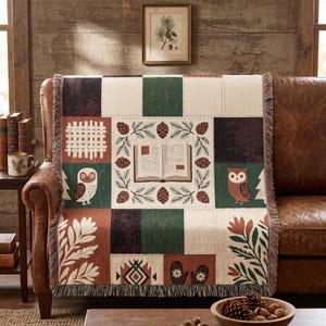 Könnte beinhalten: Eine gewebte Wohndecke mit Patchwork-Design in Creme, Waldgrün und Terrakotta. Das Muster zeigt Illustrationen eines offenen Buches, umgeben von Tannenzapfen, Eulen, Fäustlingen und botanischen Motiven mit gefransten Rändern.