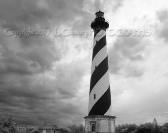 May include: A black and white striped lighthouse stands tall against a cloudy sky. The lighthouse is surrounded by grass and a brick path leads away from it.