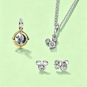 May include: Jewelry set featuring a gold and silver pendant with a Mickey and Minnie Mouse design, a silver necklace with a Mickey Mouse pendant, and two pairs of Mickey Mouse earrings. The earrings have heart-shaped accents.