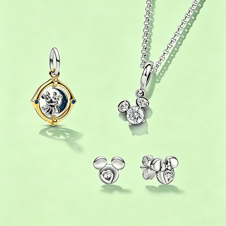 May include: Jewelry set featuring a gold and silver pendant with a Mickey and Minnie Mouse design, a silver necklace with a Mickey Mouse pendant, and two pairs of Mickey Mouse earrings. The earrings have heart-shaped accents.
