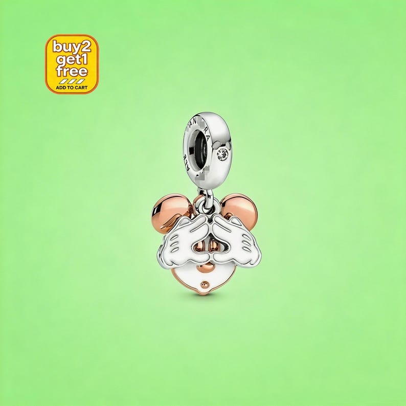 May include: A silver and rose gold-toned charm featuring a cartoon character face with white gloved hands covering the eyes. The charm includes a circular bail with a small embedded stone and the text buy 2 get 1 free add to cart.