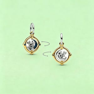 May include: Two-sided gold-toned pendant with a silver-colored design of a couple dancing in front of a crescent moon. The pendant has a square shape with blue accents and a silver-colored bail.