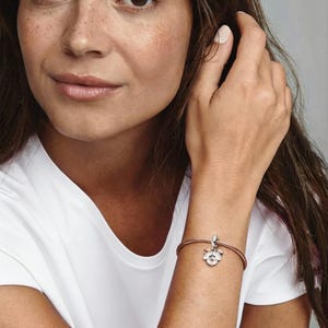 May include: A rose-gold tone snake chain bracelet featuring a singular charm shaped like a three-petaled flower. The charm is crafted with a metallic finish and includes small, clear, sparkling stones embedded within the center of each petal.