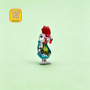 May include: A silver charm shaped like a cartoon chicken with a bright red comb, large white eyes, and a body featuring iridescent green and blue enamel detailing. The charm has a small loop at the top and stands on two detailed silver feet.