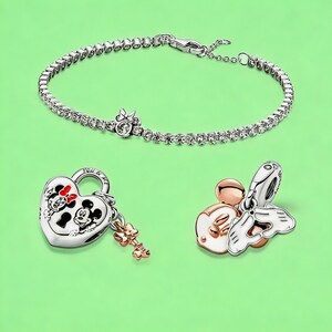 May include: A silver-tone tennis bracelet with a small bow charm, a heart-shaped padlock charm featuring Mickey and Minnie Mouse with the text YOU & ME and a small key, and a charm depicting Mickey Mouse ears with white enamel and hands forming a heart.
