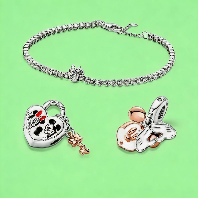 May include: A silver-tone tennis bracelet with a small bow charm, a heart-shaped padlock charm featuring Mickey and Minnie Mouse with the text YOU & ME and a small key, and a charm depicting Mickey Mouse ears with white enamel and hands forming a heart.