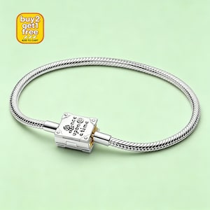 May include: A silver bracelet with a snake chain design. The clasp is a square shape with the words "once upon a time" engraved on it. A small diamond is set in the clasp. The background is a light green color.