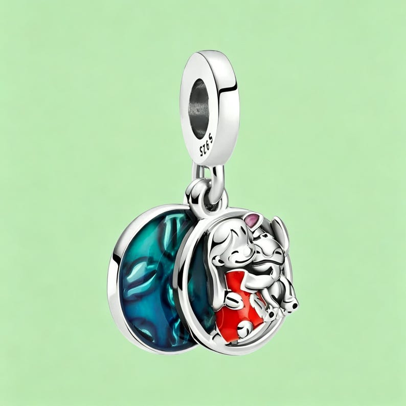 May include: A silver charm with a blue and teal enamel design and a cartoon image of two characters. One character is wearing a red outfit. The charm has a loop at the top for attaching to a bracelet or necklace.
