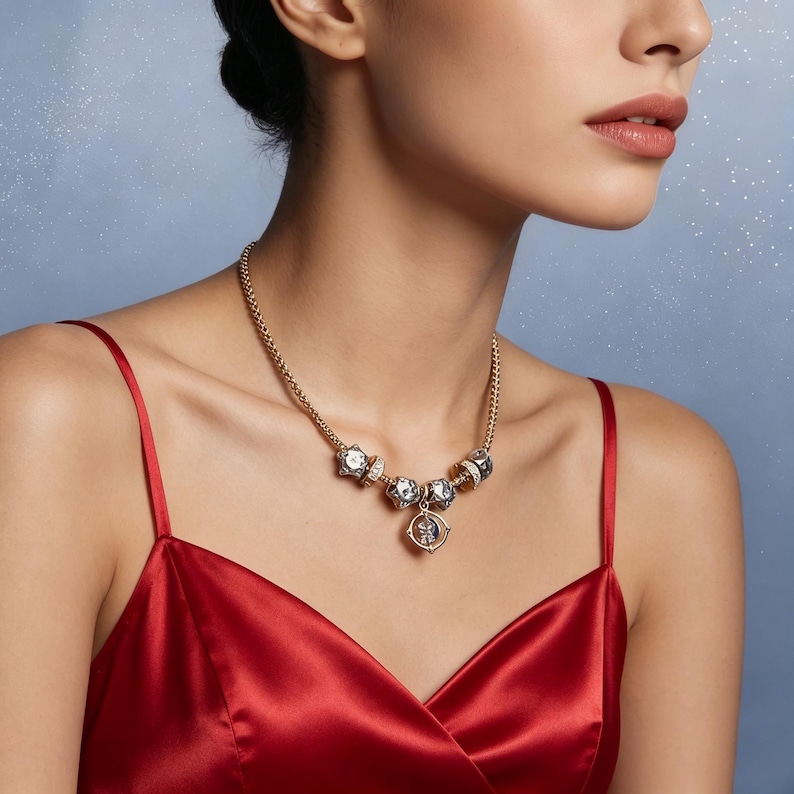 May include: A gold-toned necklace with multiple clear and silver-toned beads and a pendant. The necklace is worn against a red satin dress. The background is a light blue with small white specks.
