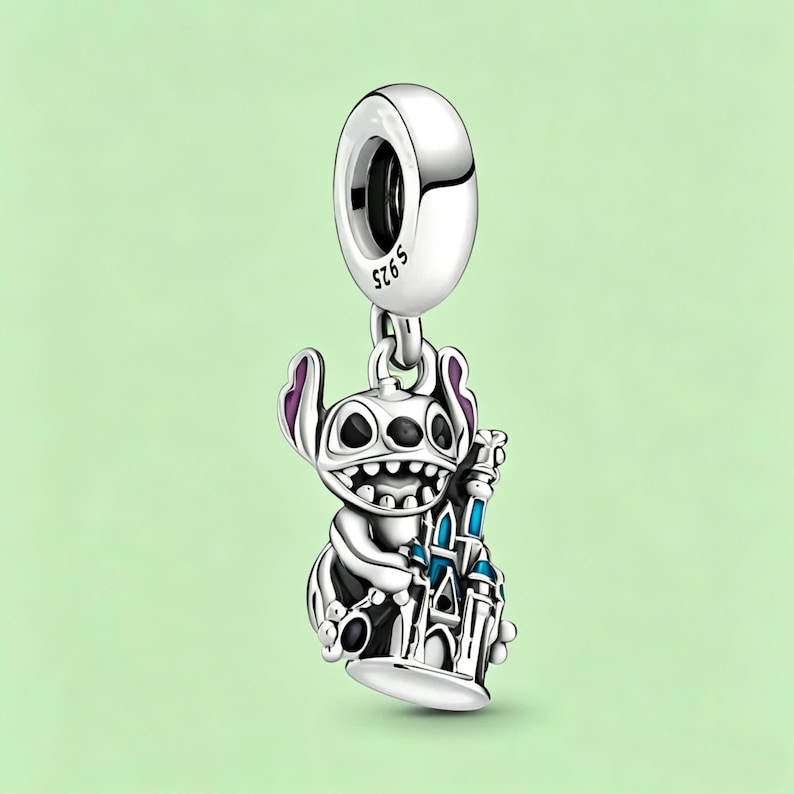 May include: A silver charm featuring the character Stitch from Lilo & Stitch, holding a blue and white castle. The charm has purple accents on Stitch's ears and is suspended from a silver loop.