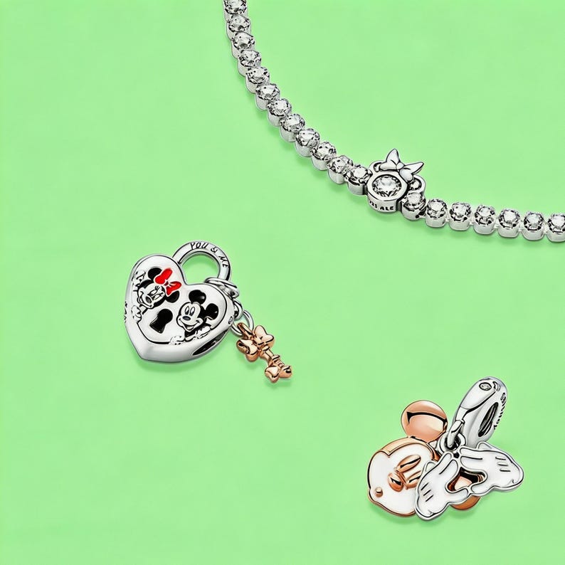 May include: A silver tennis bracelet with clear stones and a Minnie Mouse bow charm, a heart-shaped padlock charm featuring Mickey and Minnie Mouse with a small rose gold key, and a rose gold and silver charm depicting Mickey Mouse hands forming a heart.