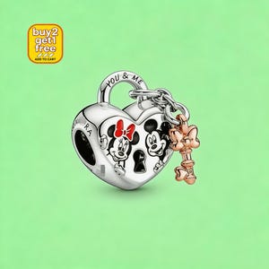 May include: A silver heart-shaped charm featuring a black and white illustration of Mickey and Minnie Mouse with a red bow. The charm has a keyhole design, the text YOU & ME engraved on the top, and a small rose gold-toned key charm attached to it.