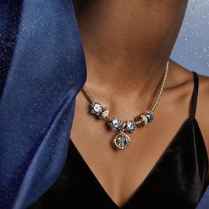 May include: A gold-toned chain necklace featuring multiple charms, including several silver-toned star-shaped beads and a central circular pendant with a rotating moon and star design, accented with small clear stones along the chain links.