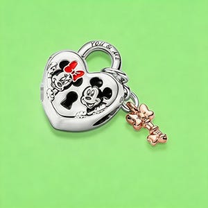 May include: A silver heart-shaped padlock charm featuring engraved images of Mickey and Minnie Mouse with black and red enamel details. The top of the padlock is inscribed with the text YOU & ME. A small rose gold-toned key charm hangs from the side.