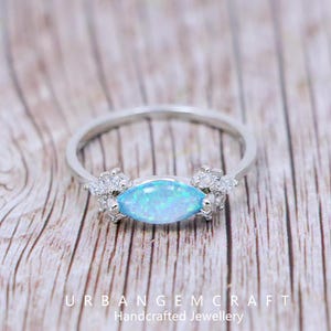 May include: A silver ring with a light blue marquise-cut opal as the central stone. The ring is embellished with small, clear gemstones. The text "URBANGEMCRAFT Handcrafted Jewellery" is visible.