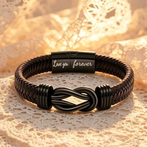 May include: A dark brown braided bracelet featuring a black metal infinity knot centerpiece and a black magnetic clasp engraved with the text Love you forever. The bracelet has a textured woven band and smooth black metal accents on both sides.