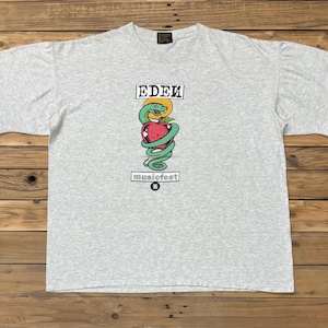May include: A light gray t-shirt featuring a graphic of a red apple entwined by a green snake, with the text "EDEN" above and "musicfest 96" below. The shirt is made of a soft material.
